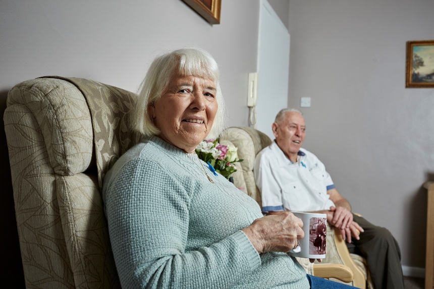Woman looking lovingly at man sitting in an armchair holding a walking stick