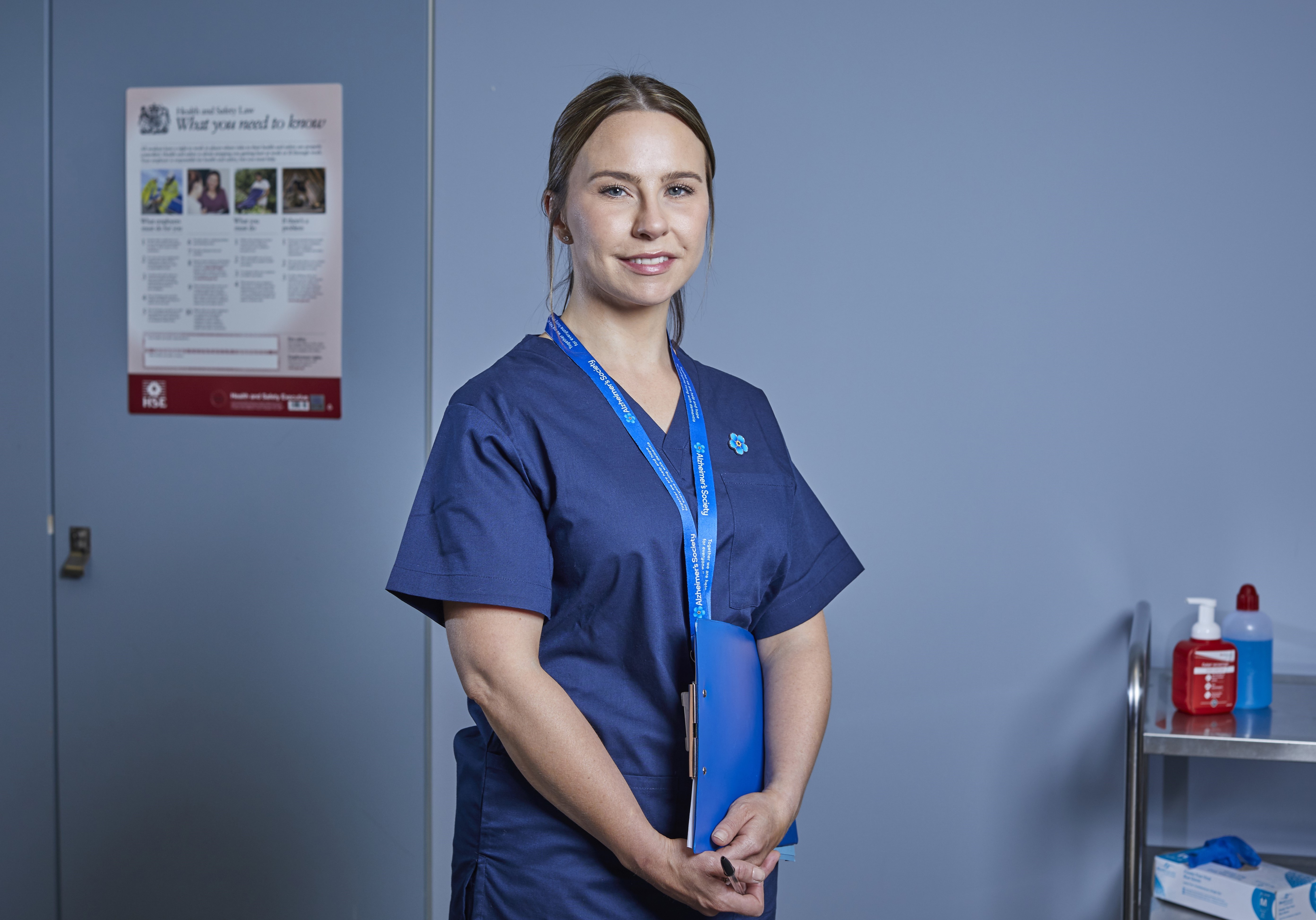 a woman in nursing scrubs stands in her practice and smiles.