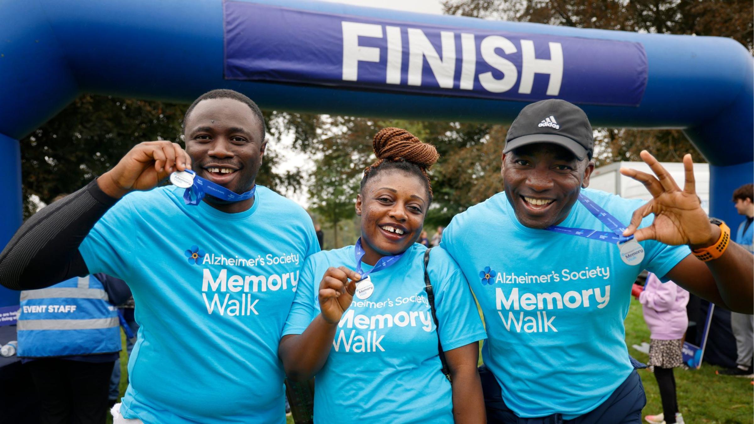 3 people in blue Memory Walk t-shirts smiling and holding up their medals