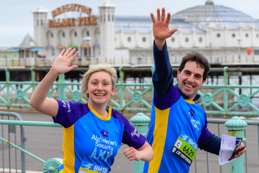 Two Alzheimer's Society Runners waving as they pass Brighton Pier