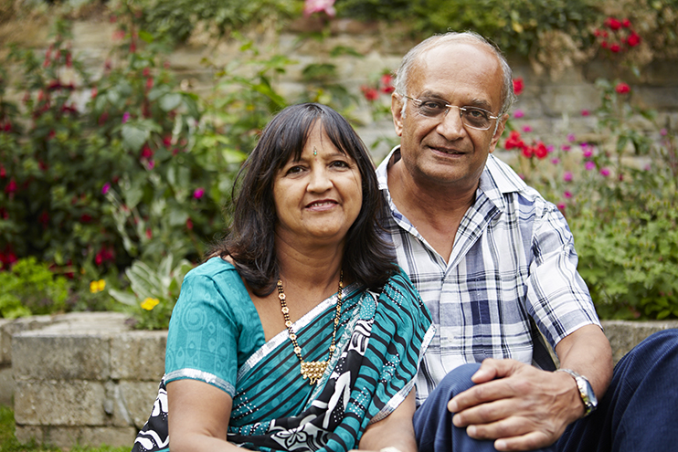 A couple sit together in a garden smiling to camera