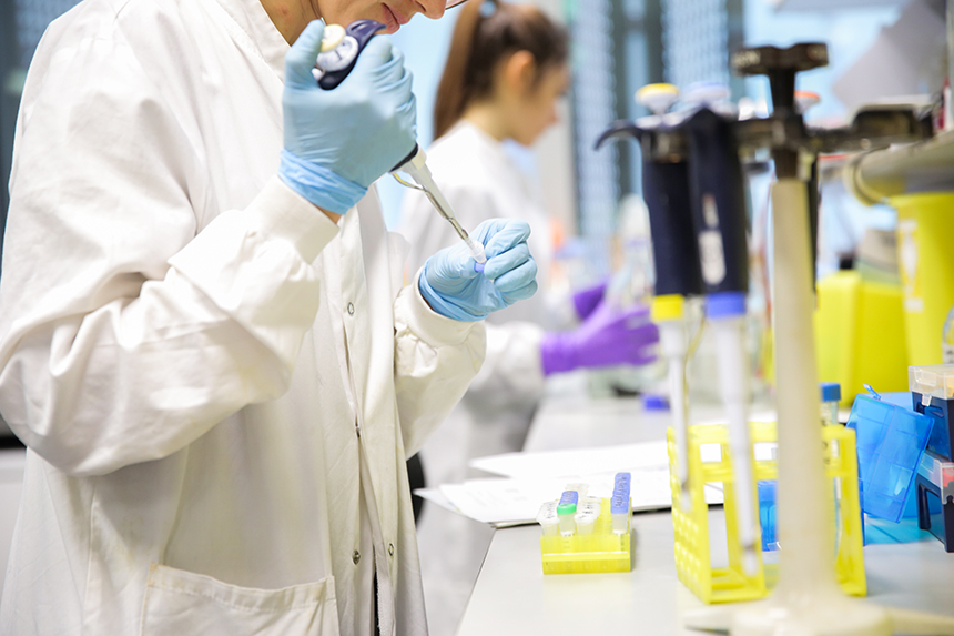 Researchers in white coats stand at lab benches performing experiments