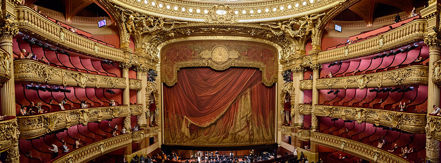 A theatre stage elaborately decorated with gold details and red velvet curtains