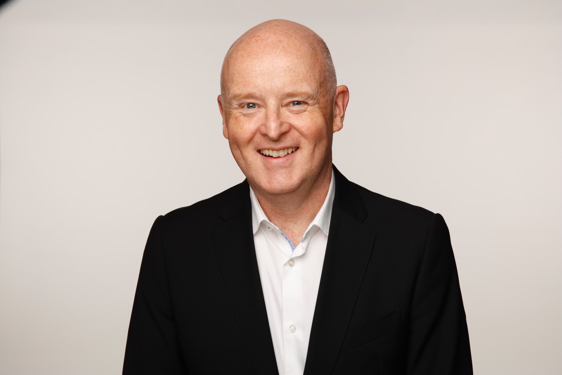 A bald man smiling wearing a white shirt and black blazer