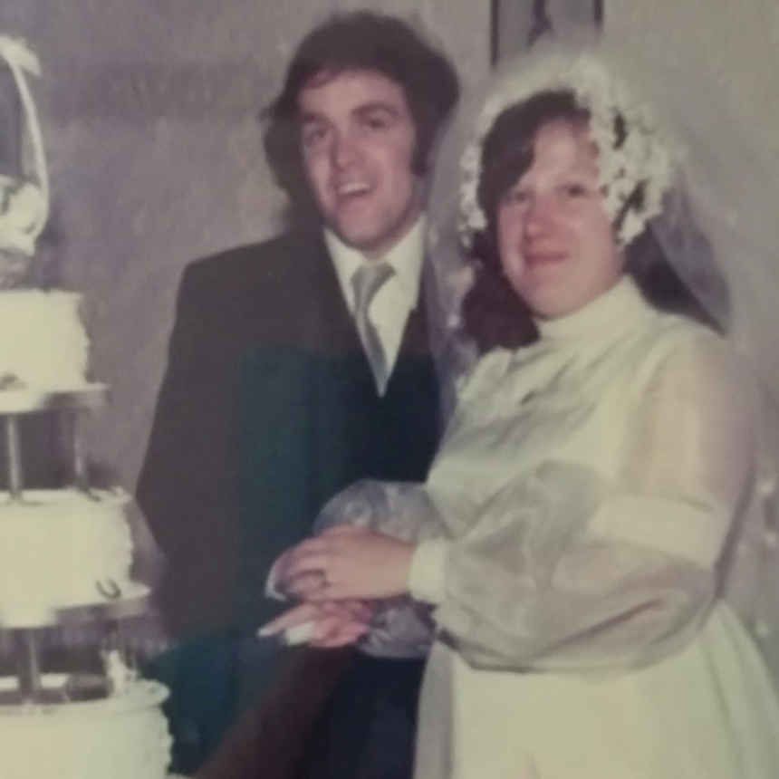 Emily and Jim on their wedding day, cutting a cake