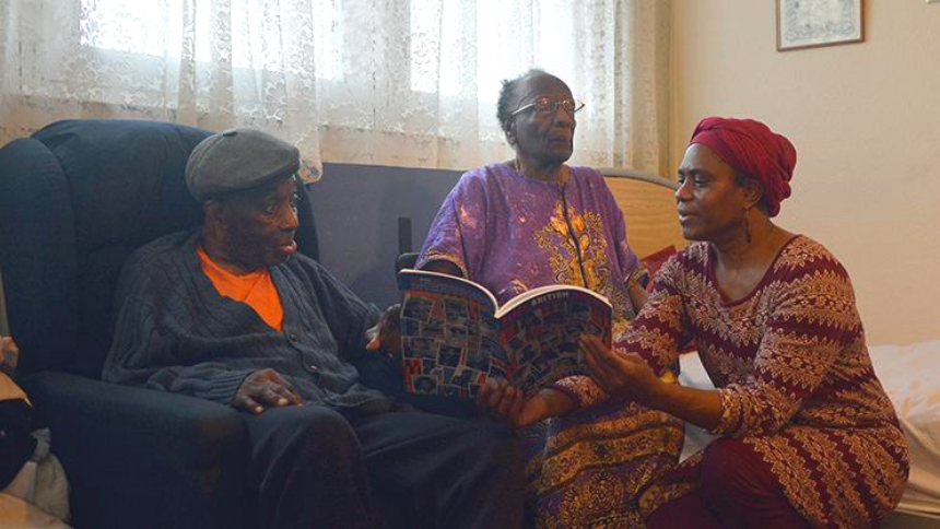 A woman kneeling down and reading a book to two men