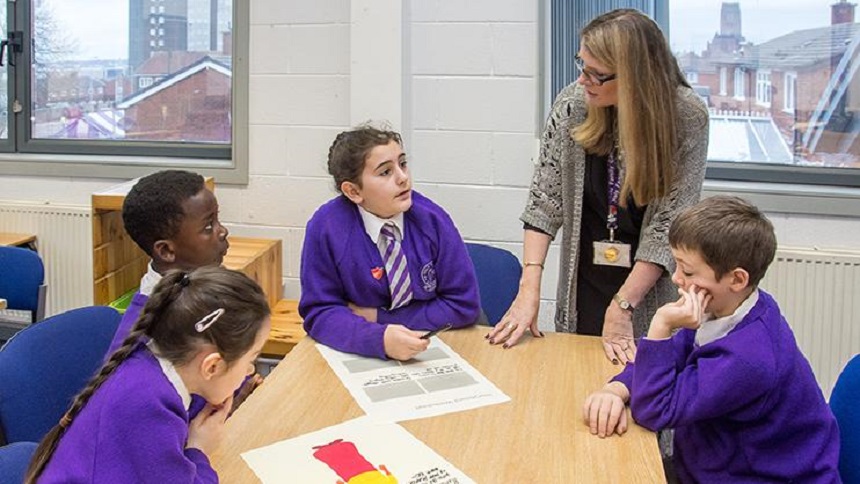 A teacher talking to four students sitting at a desk