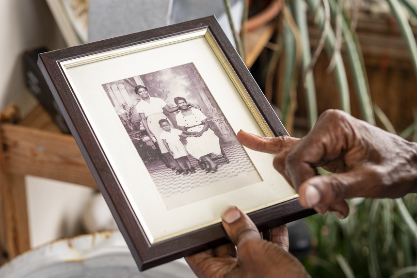 Morcea holding a frame with an old photograph of her as a child with her family, including her grandmother