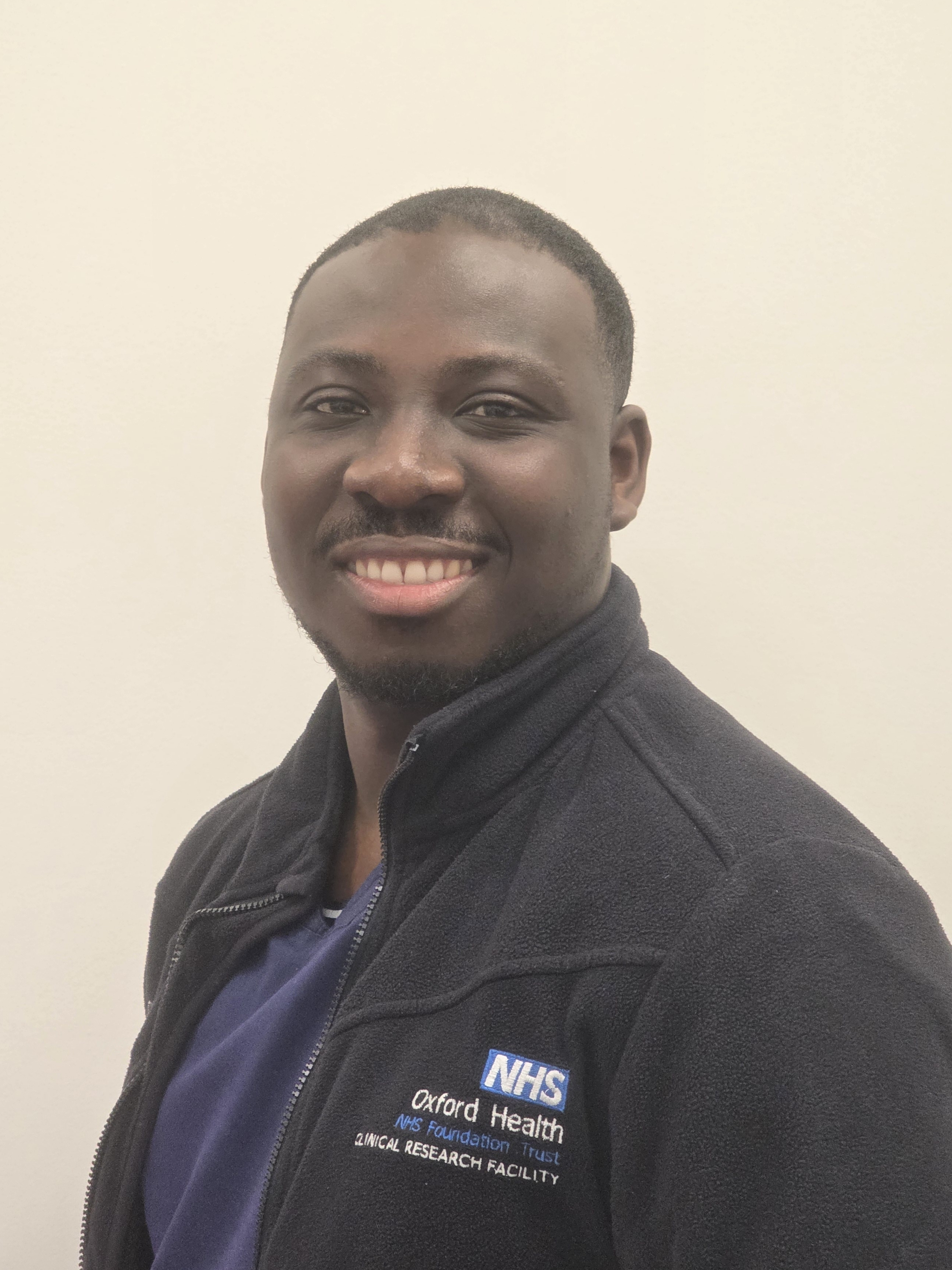 Portrait of a young man in a nurse uniform and an NHS Oxford Health fleece.