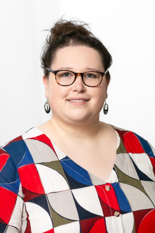 Summer Ap, wearing a red white and blue patterned top, with hair tied up and glasses, smiling