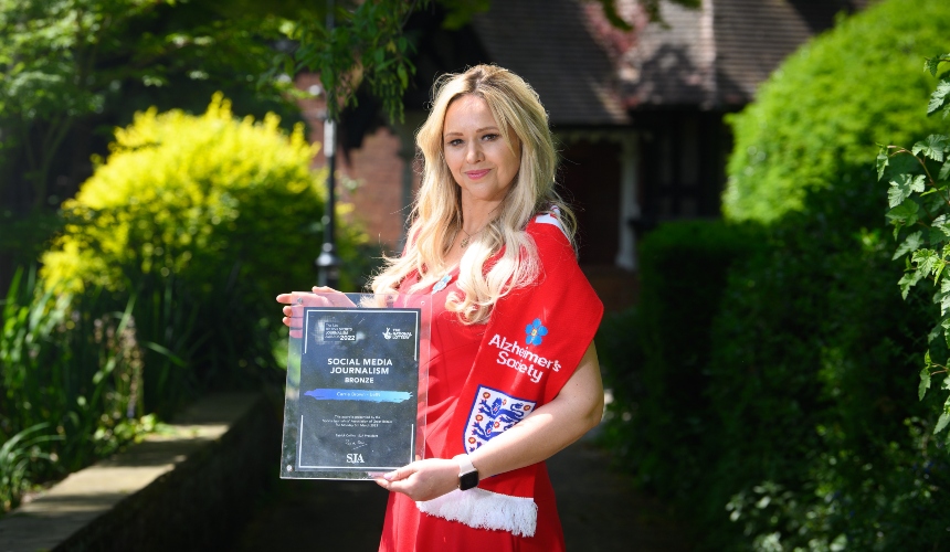 Carrie wears an Alzheimer's Society scarf, and holds up an award she received 