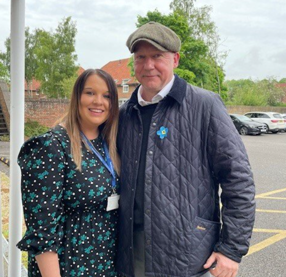 A young woman with an Alzheimer's Society lanyard stands with her arm around an older man.