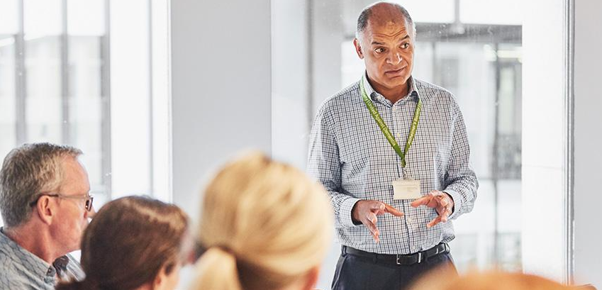 A man stands in a meeting room to speak before his colleagues. 