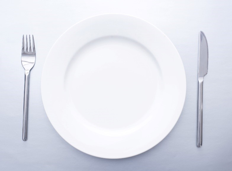 A round white plate on top of a white table with a silver knife and fork either side. Source: freefoodphotos.com