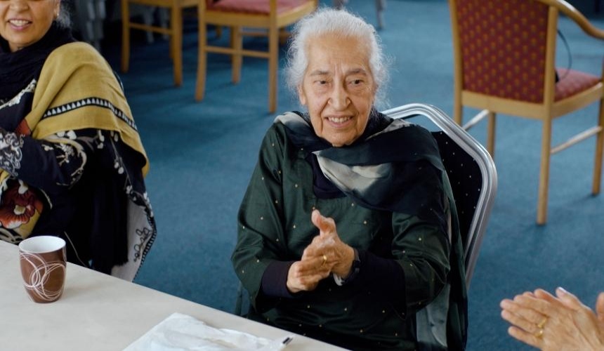 A Punjabi woman sat in a chair smiling and clapping 