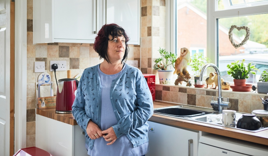 A woman stands in her kitchen, looking concerned