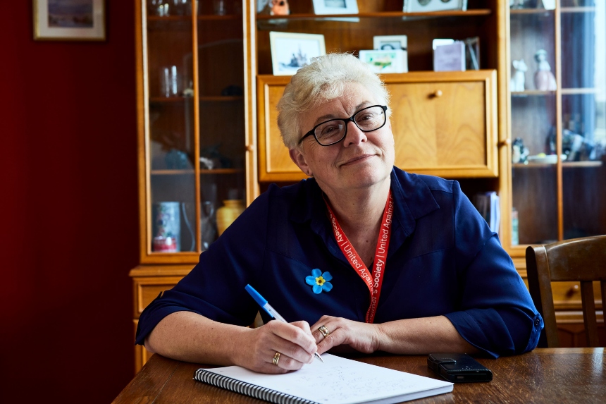 A woman wearing an Alzheimer's Society lanyard and badge sat at a table with a pen in her hand