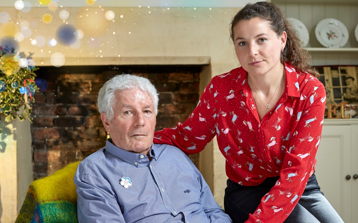 Adrian sits in a chair while Liv perches on the arm with her arm round him