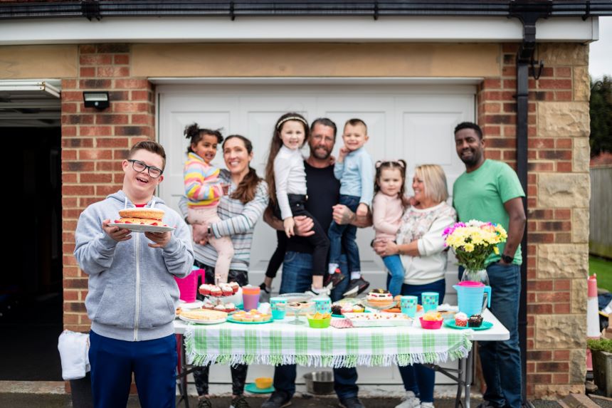 A group of people stand around a table with cake and flowers