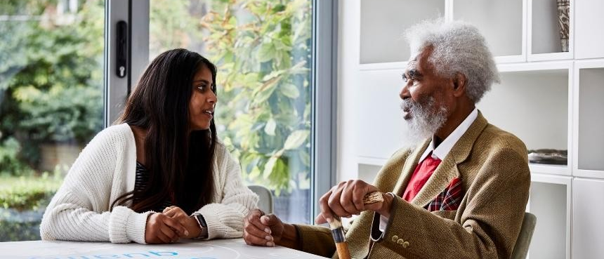 A woman woman sits an a table with an older man who holds a walking stick.