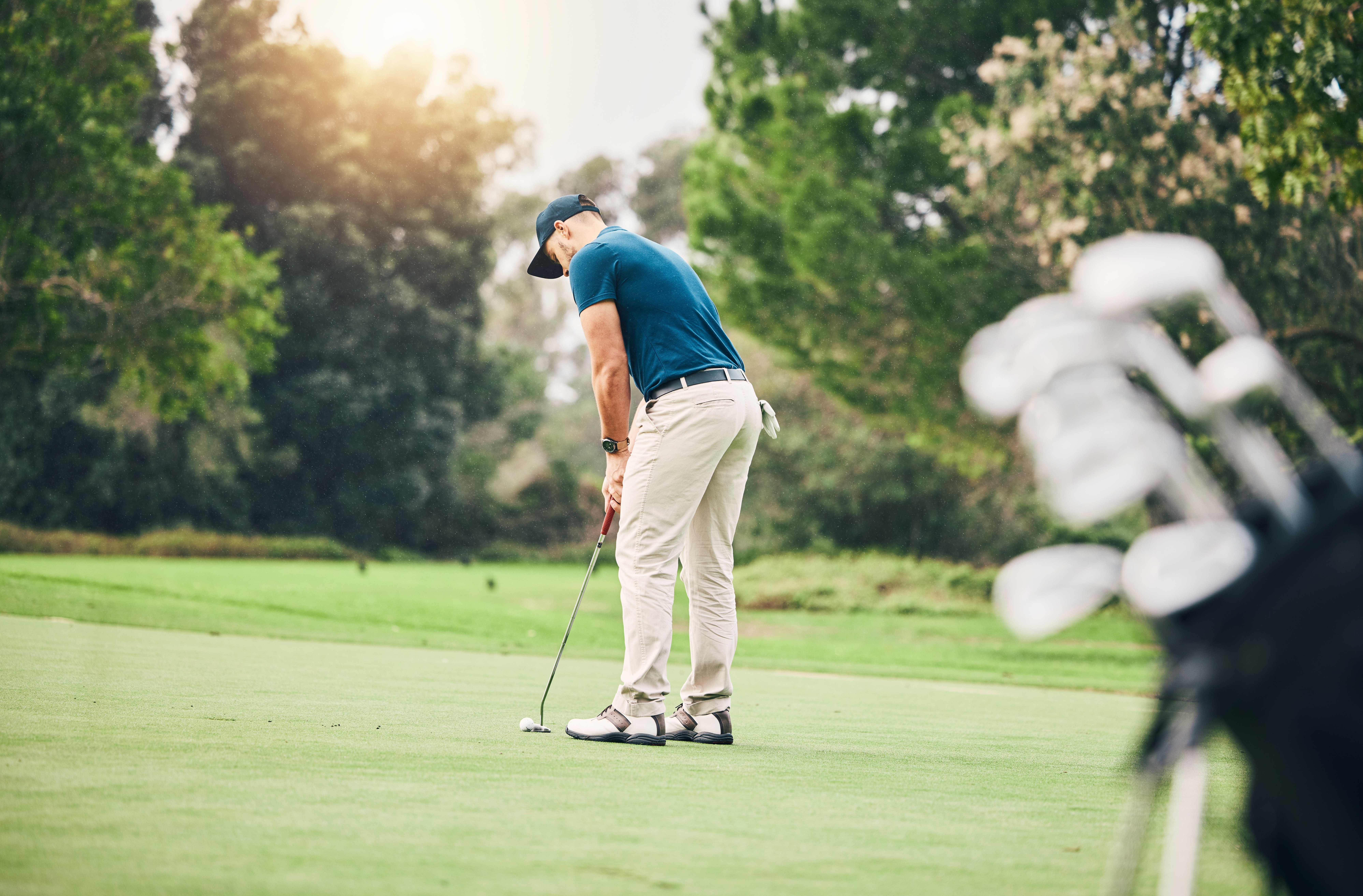 A man playing golf on the grass, surrounded by trees
