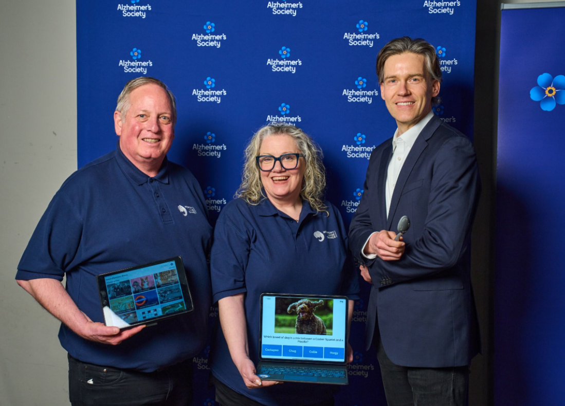 Two people hold up their laptops to a smiling man in a suit.