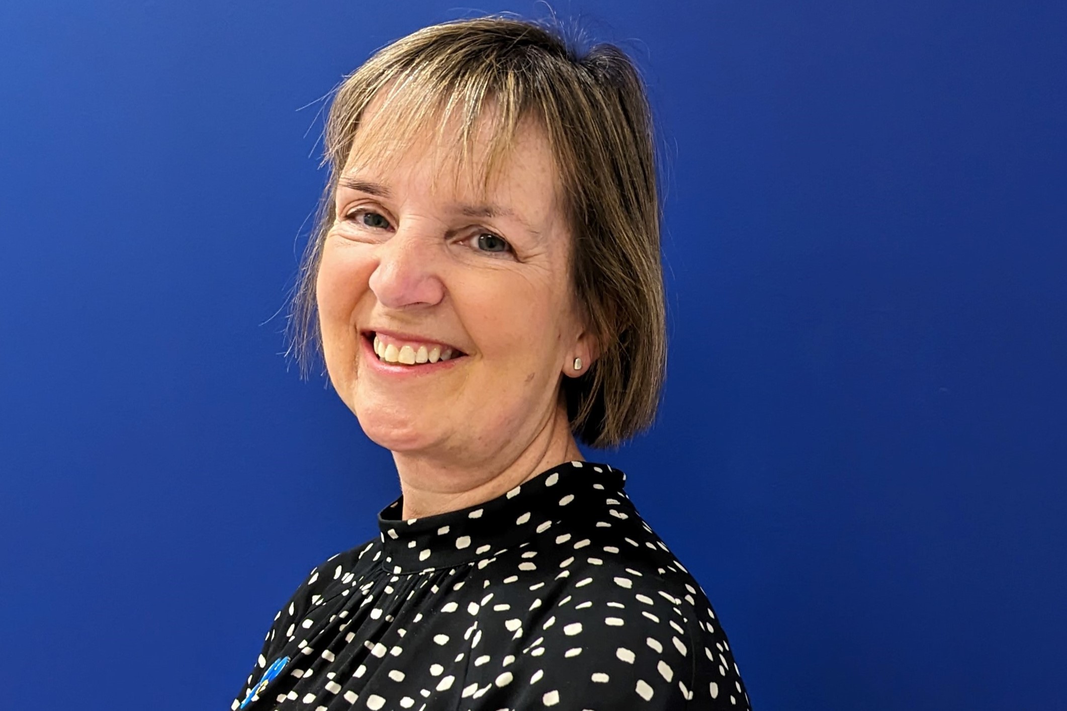 A lady with short blonde hair, smiling and wearing a black top with white dots