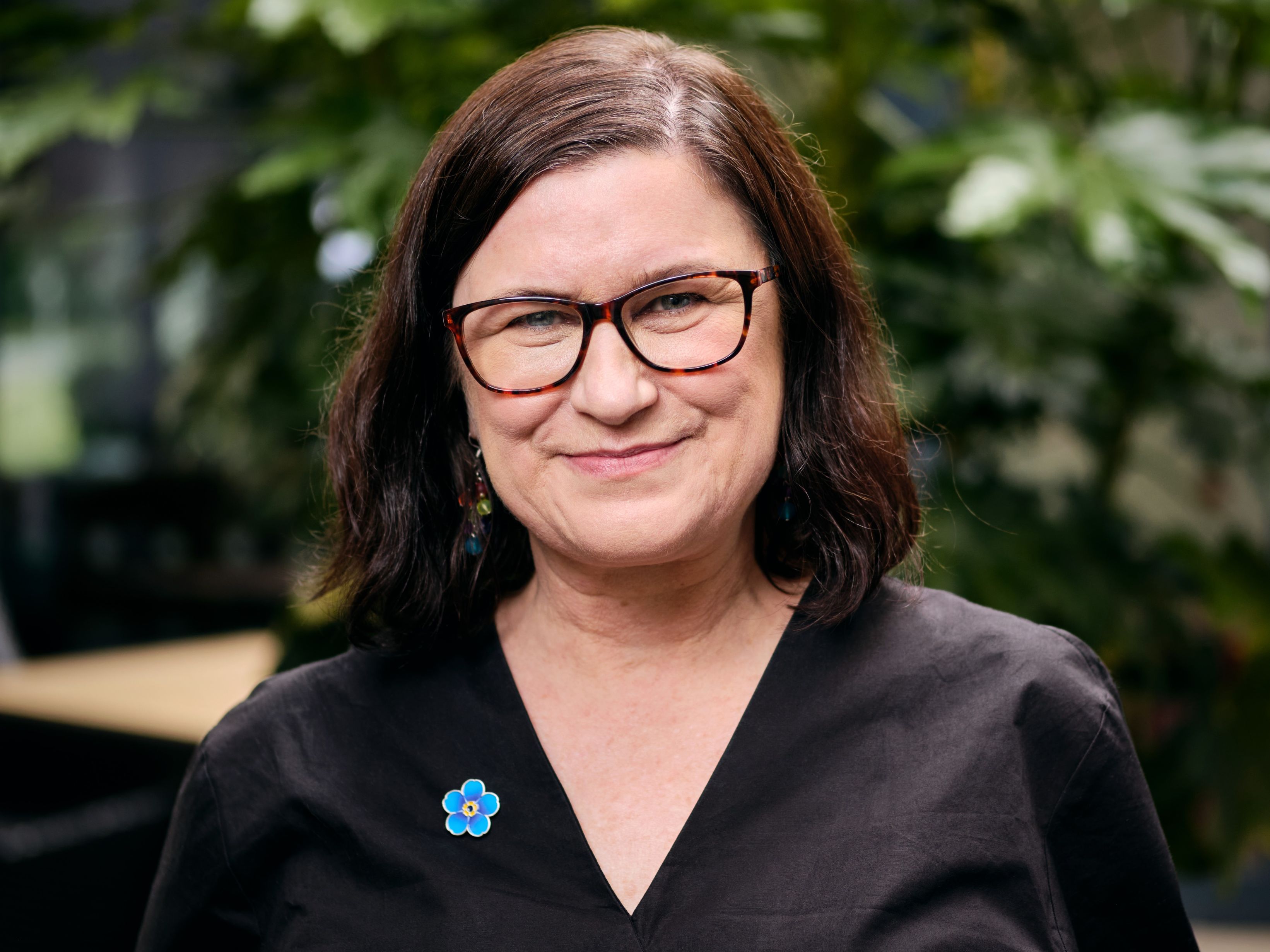 A woman with short brown hair, glasses and a black top