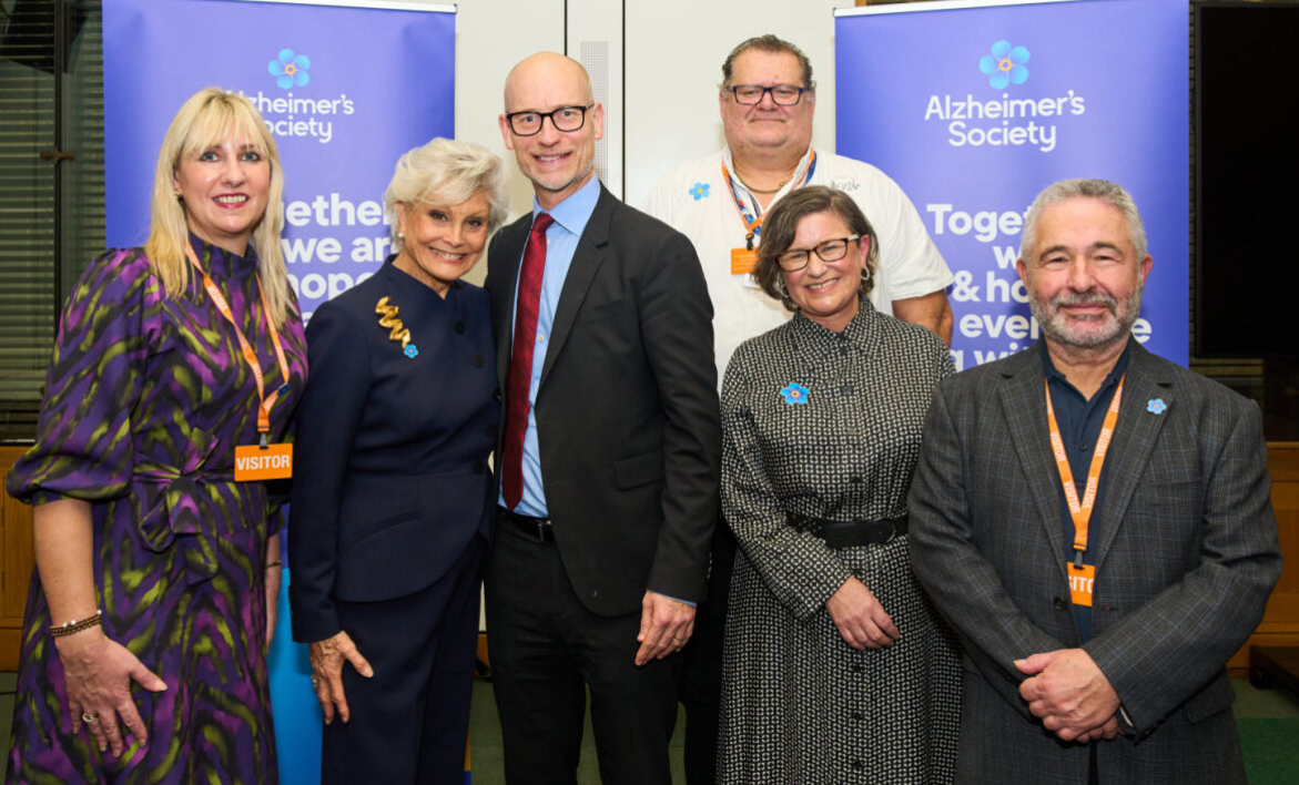 A group of people in smart dress gather in front of Alzheimer's Society banners.