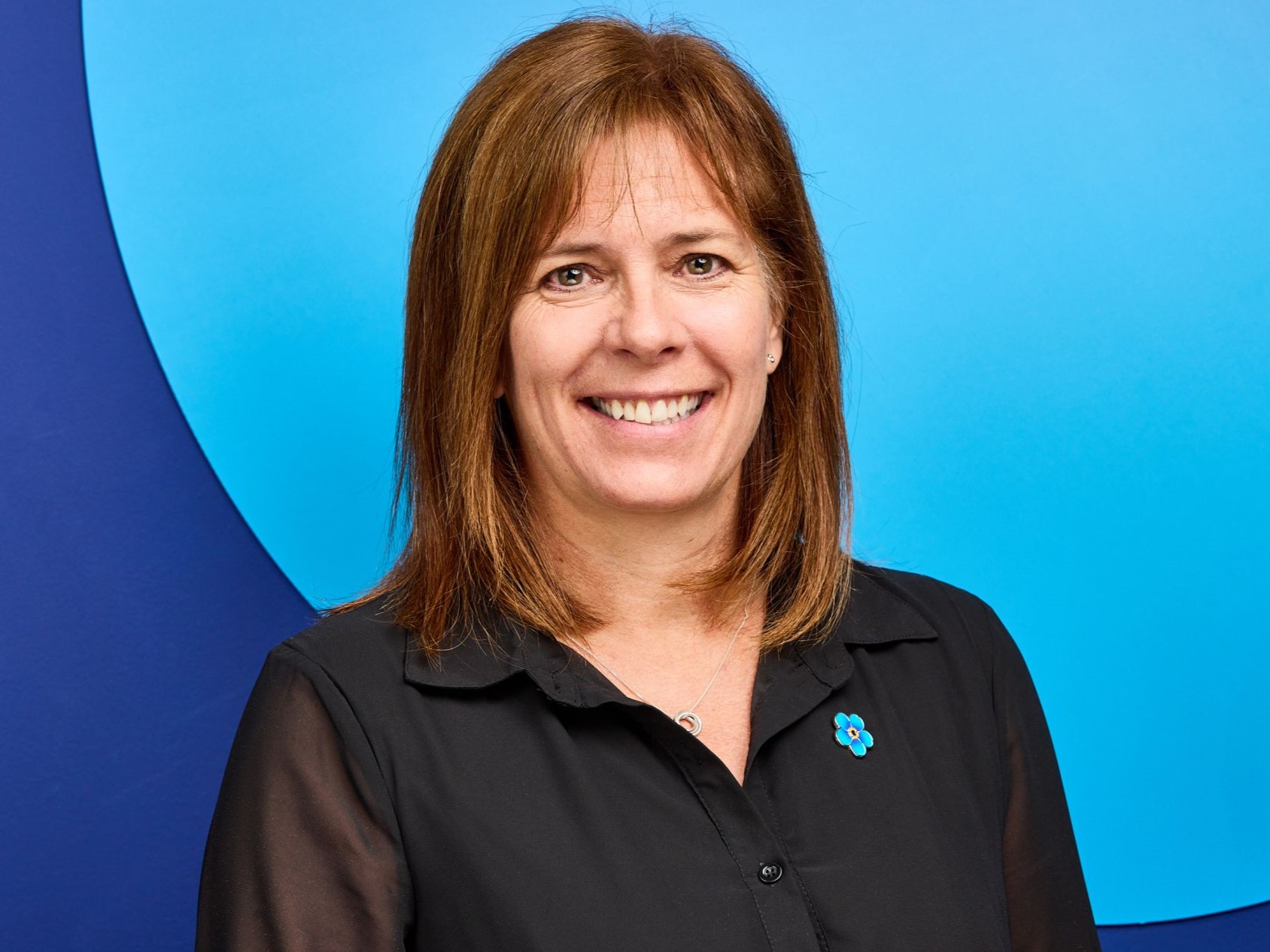 A woman with medium length brown hair who is smiling and wearing a black blouse