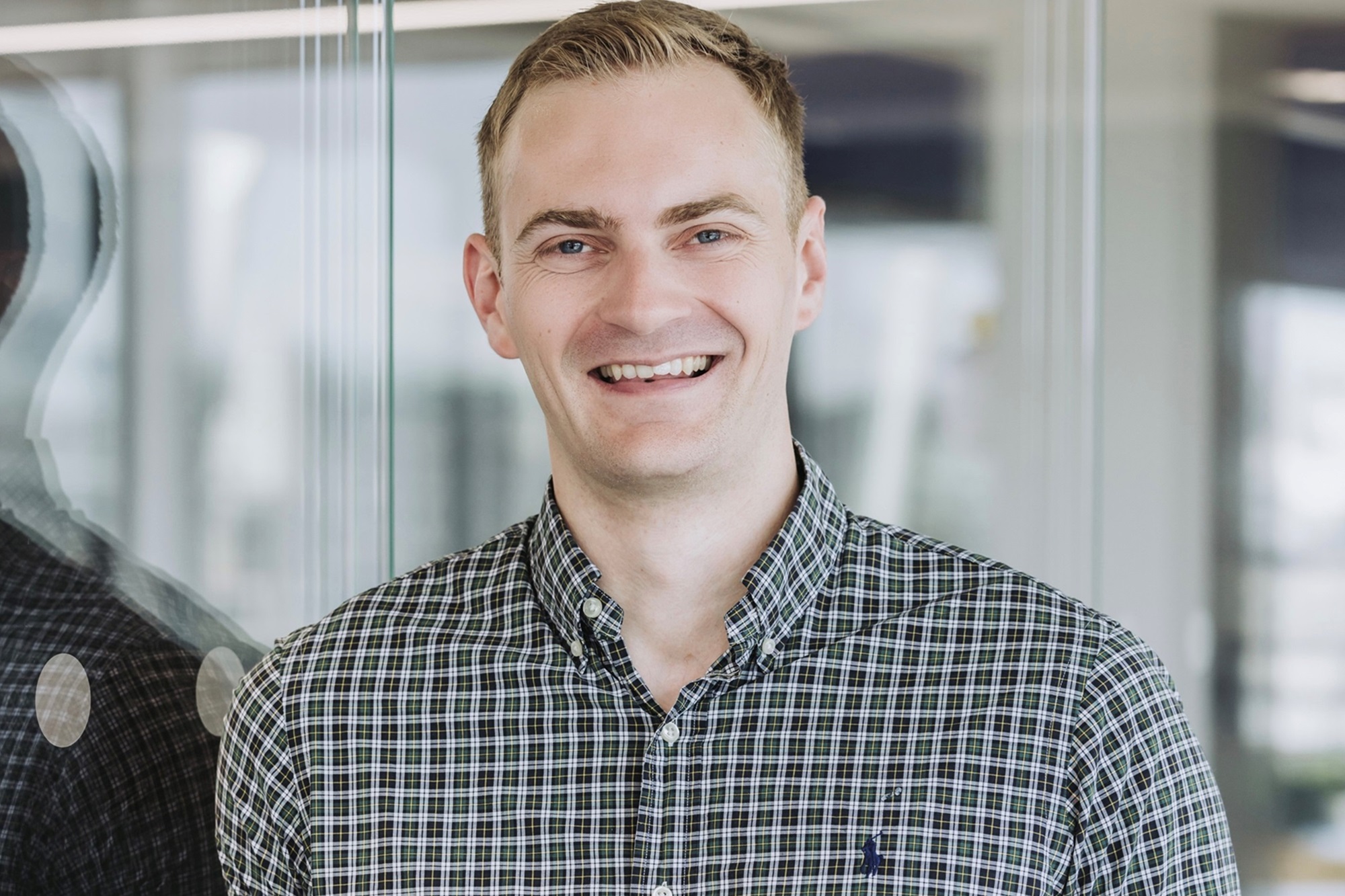 A man with short blonde hair and a dark check shirt