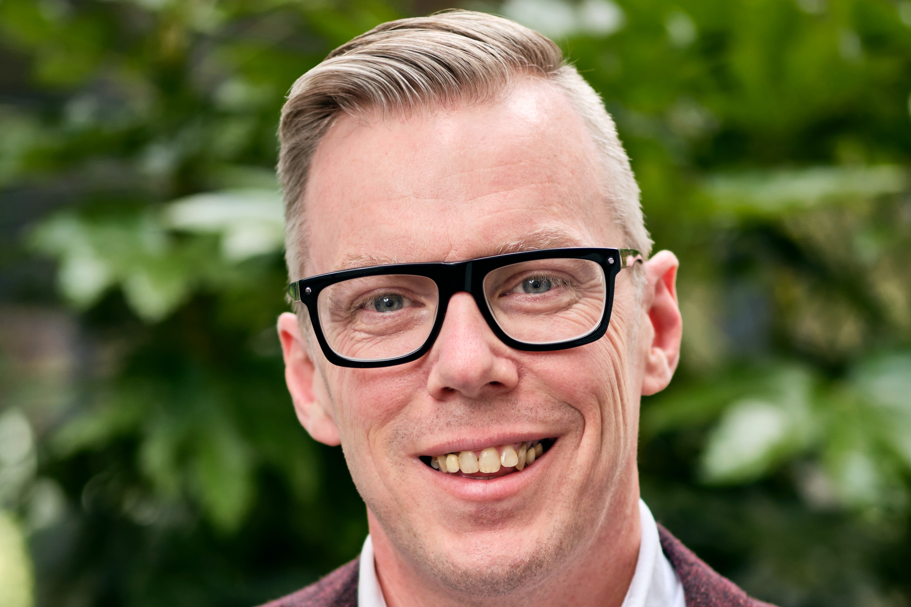 A man with short blonde hair and glasses, smiling
