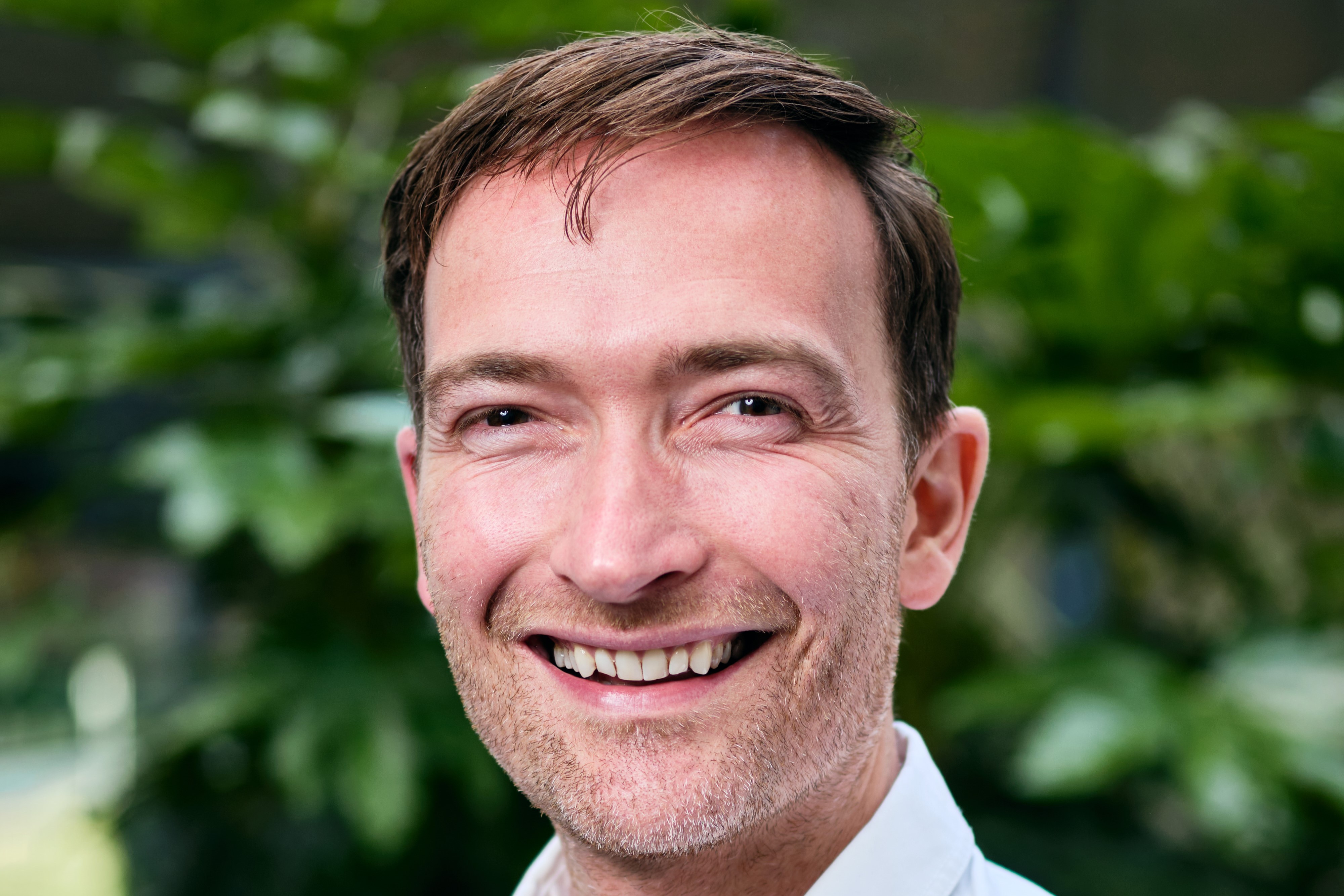A man with short brown hair and light stubble, smiling