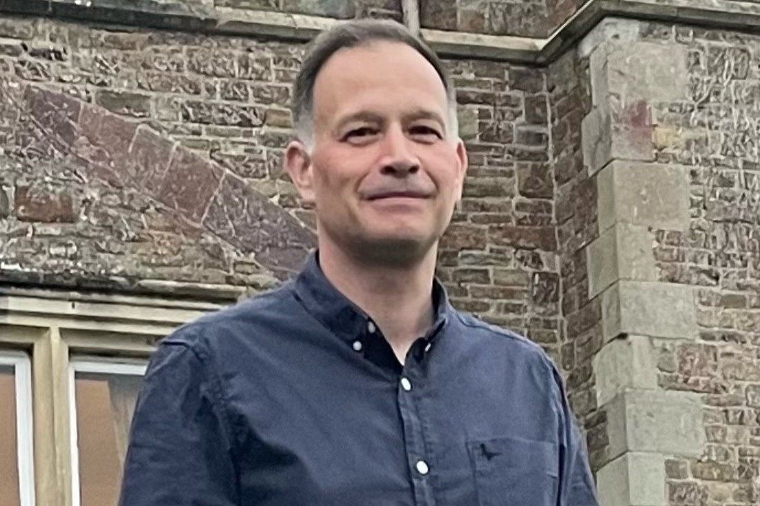A man with short dark and grey hair and a dark blue shirt