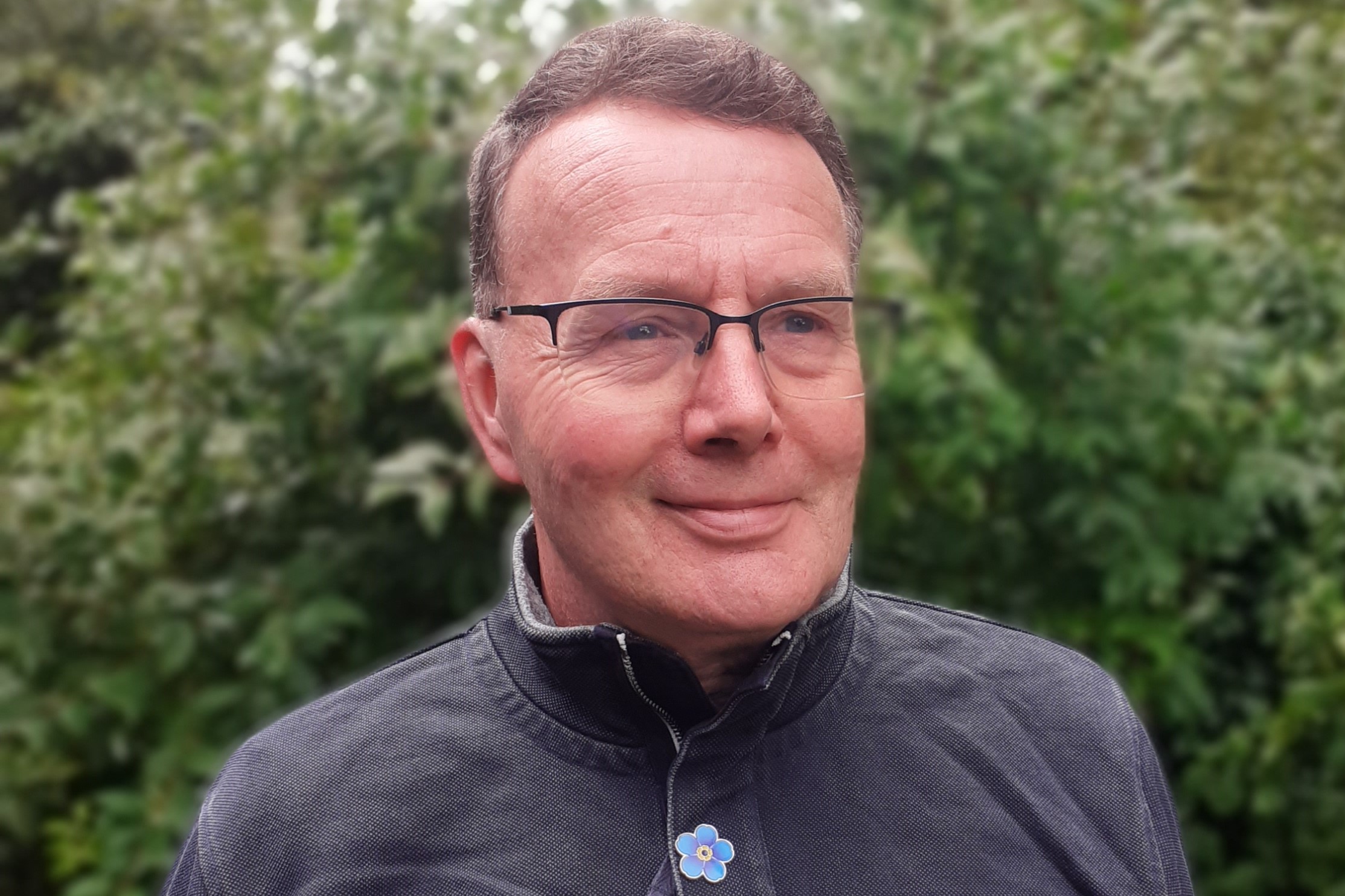 A man with short light brown hair, glasses and a grey jumper