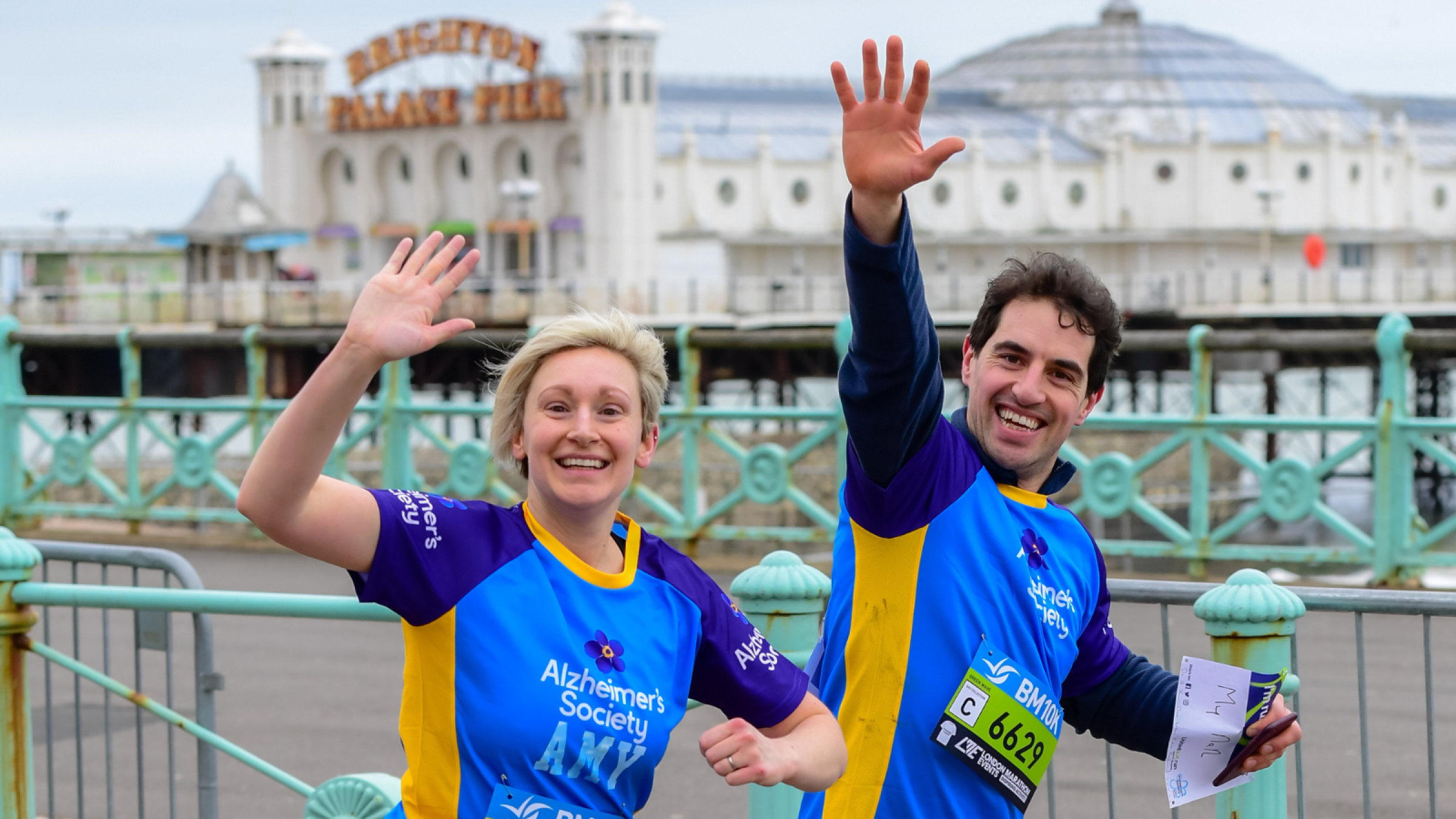 Two Alzheimer's Society runners wave as they pass Brighton Pier