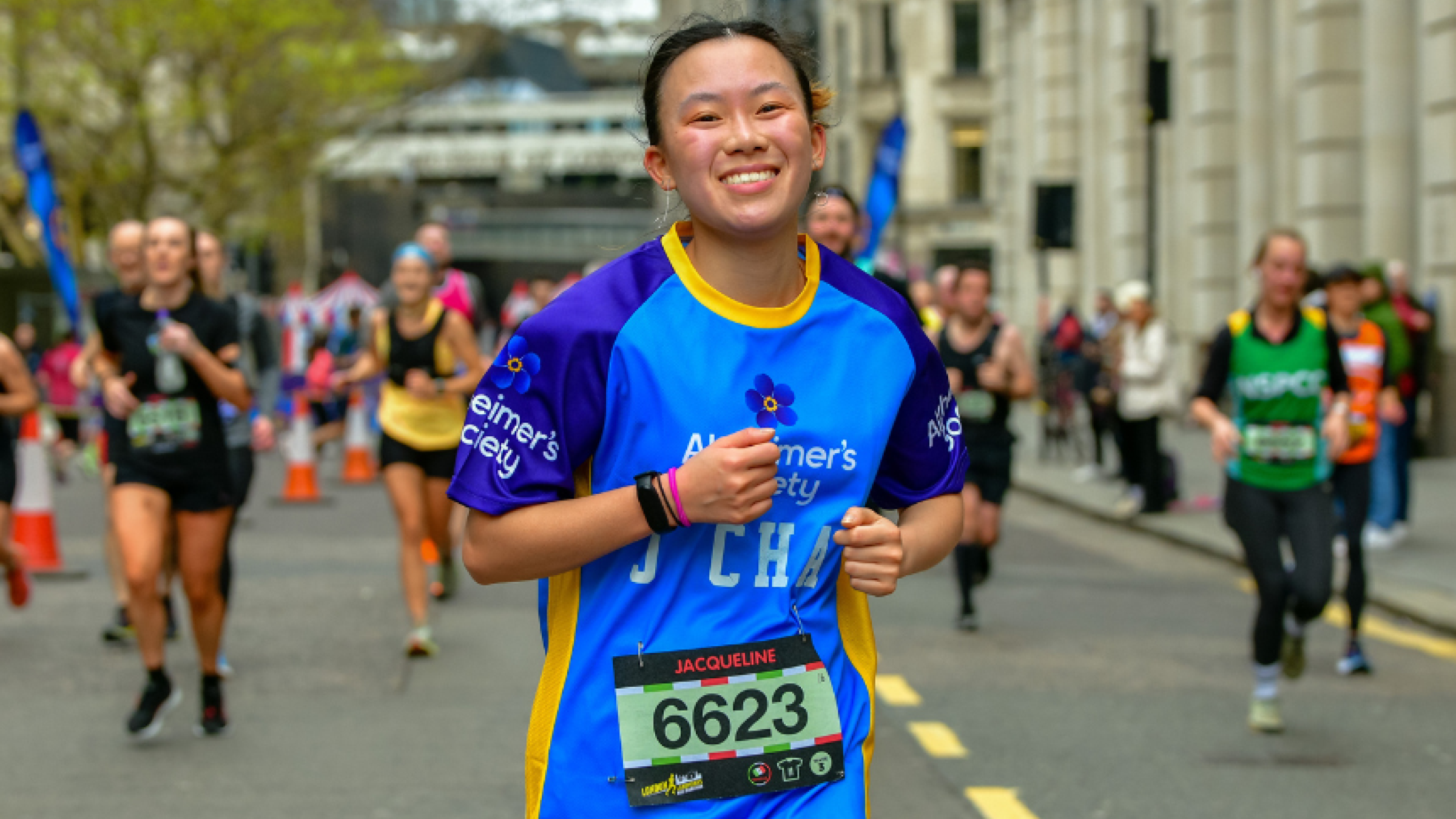 A person running ahead of a group down a city street, wearing an Alzheimers top, smiling at the camera.