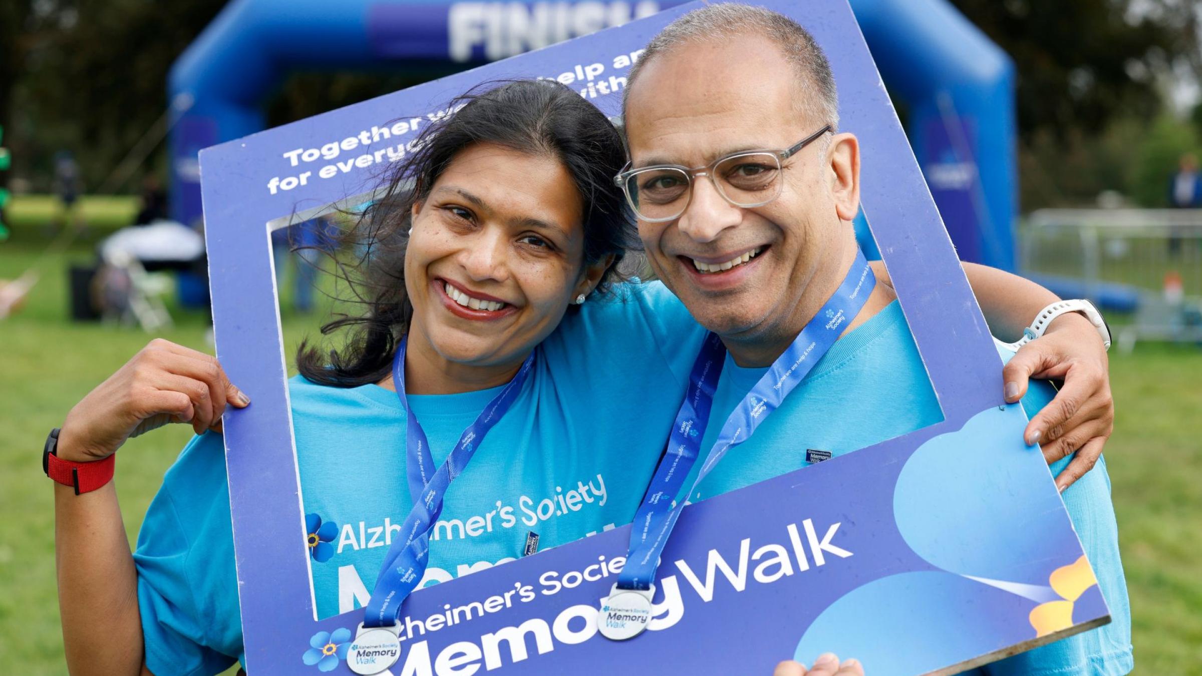 2 people smiling at the camera, wearing blue Memory Walk t-shirts and medals