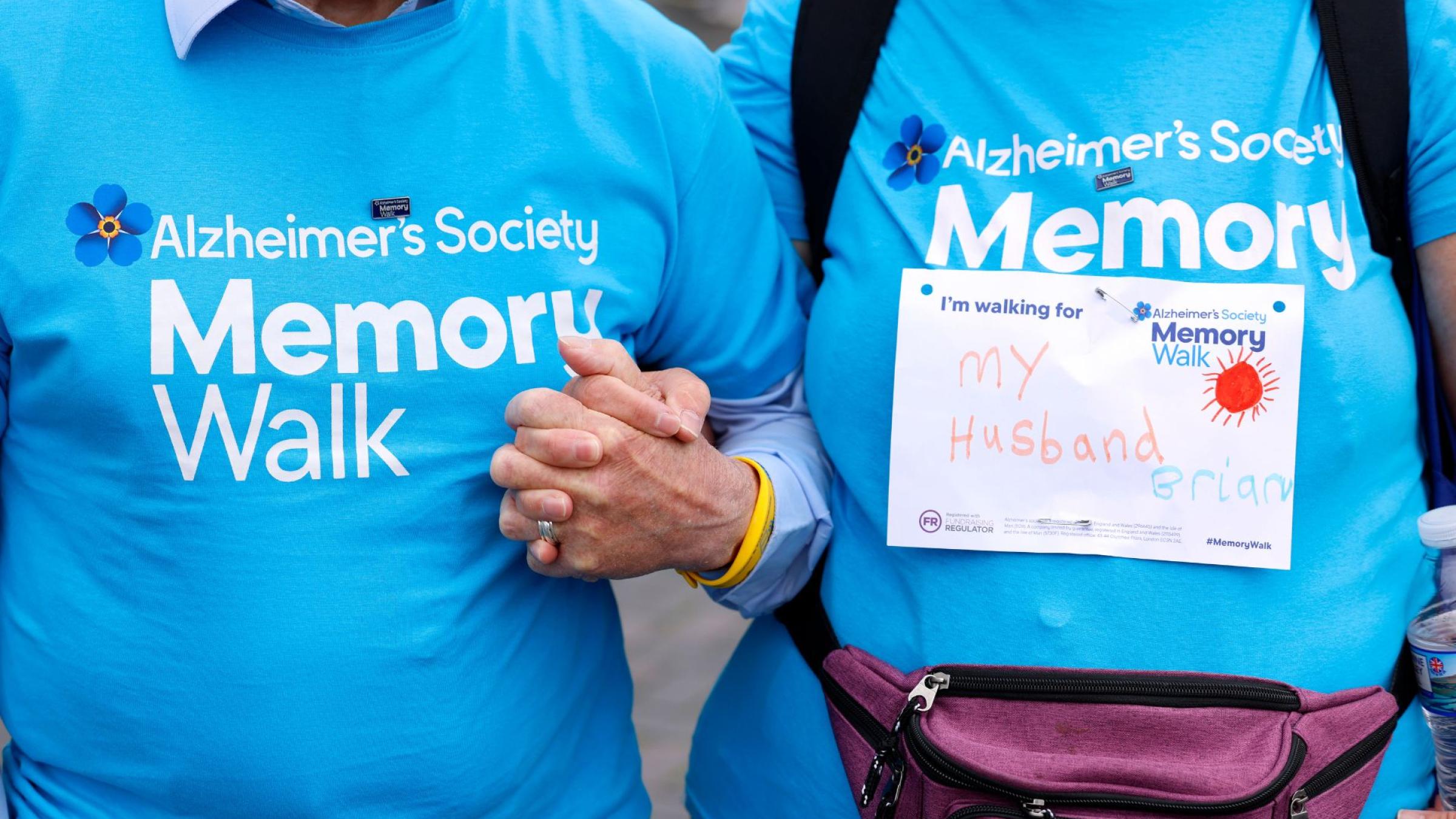 2 people holding hands, in blue Memory Walk t-shirts with a label on one saying they are walking for their husband.