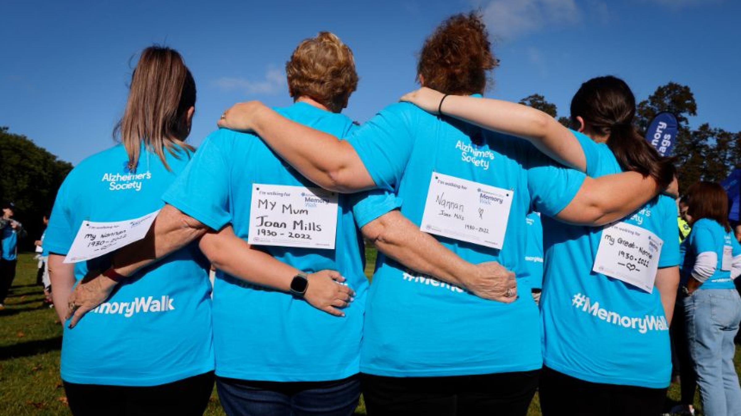 4 people arm in arm with their back to the camera, wearing blue Memory Walk t-shirts
