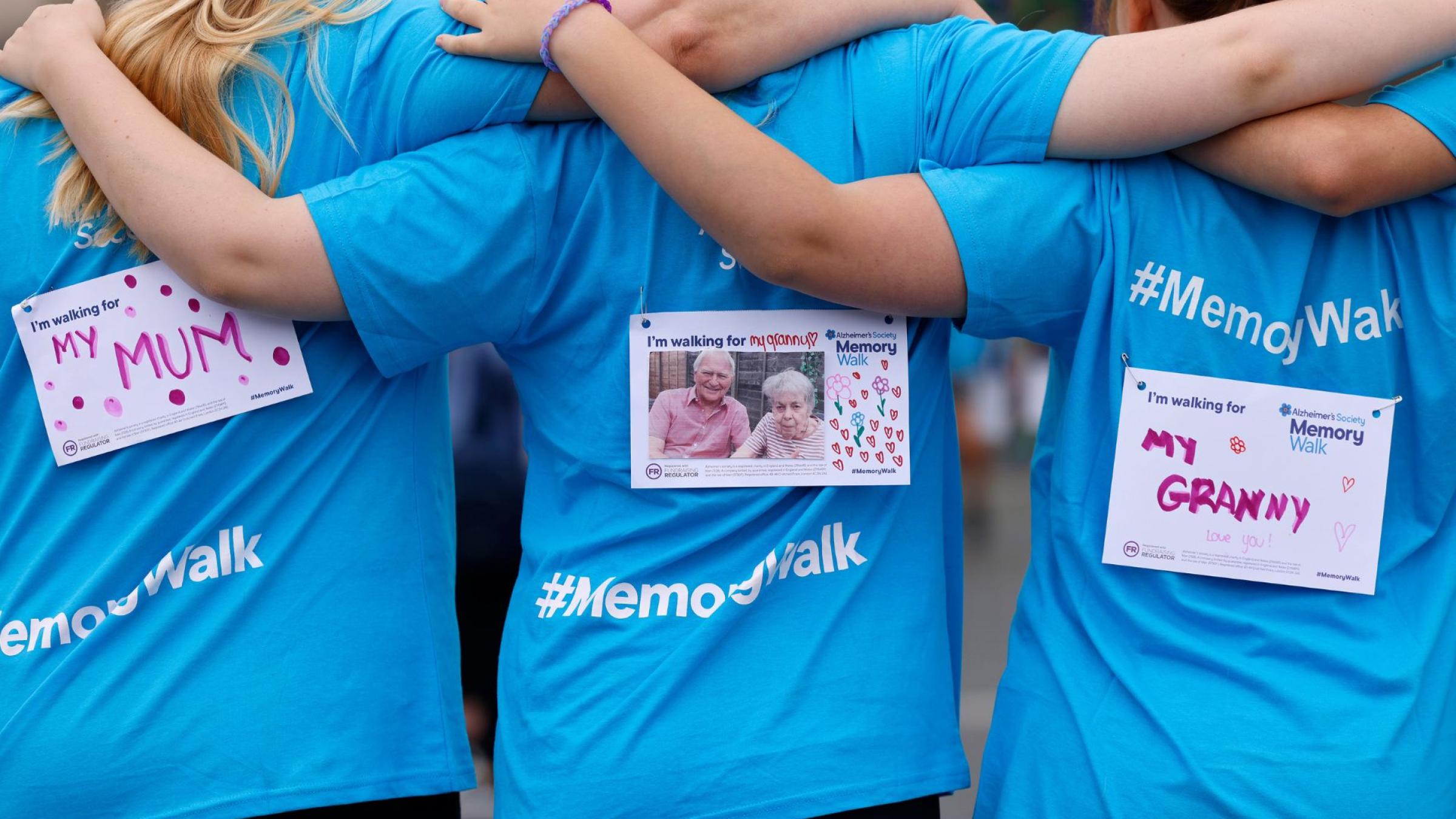 Group of three women with their backs turned and their arms around each other, in blue Memory Walk t-shirts