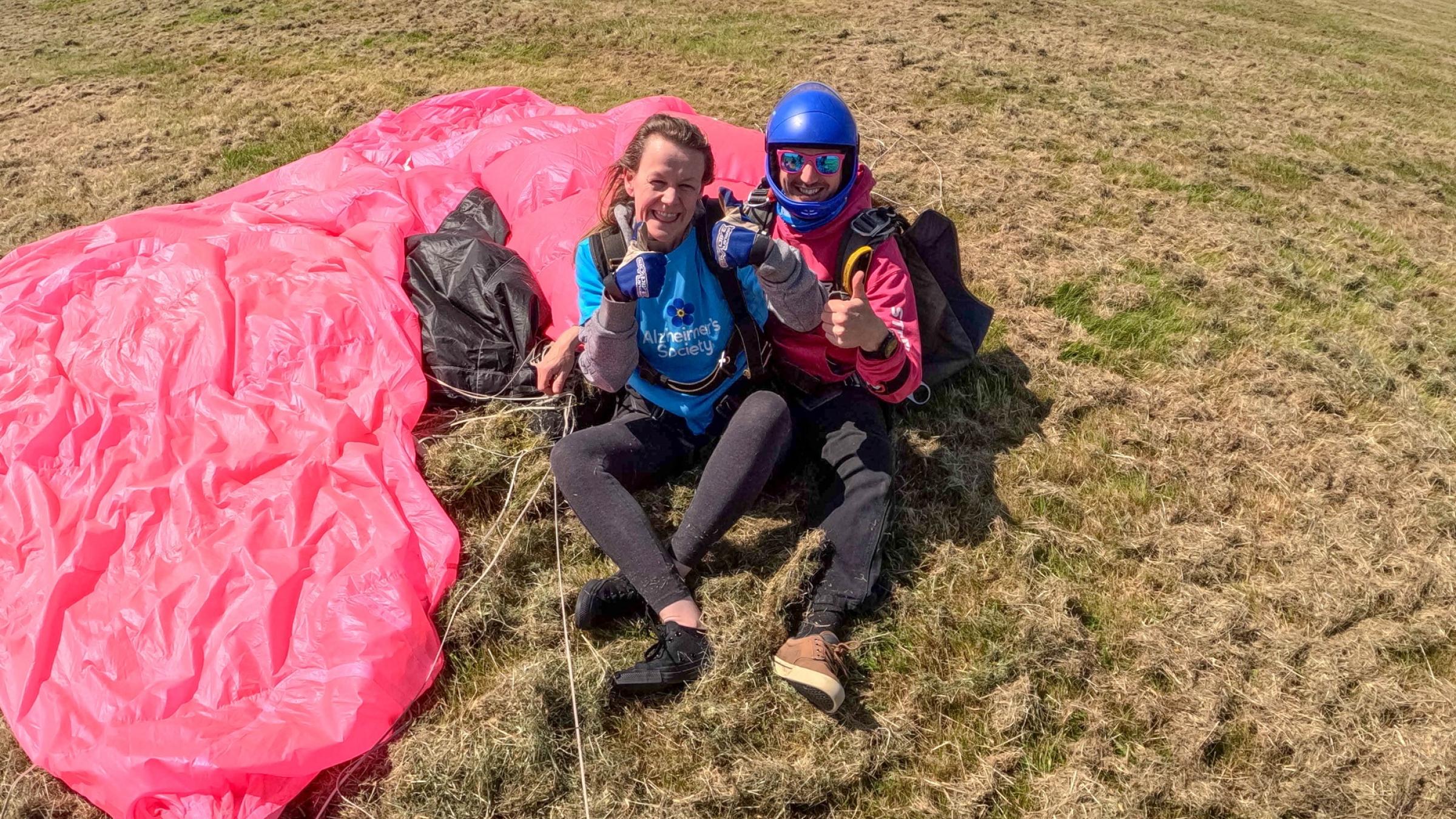 Lady and man sat on the ground by a parachute.