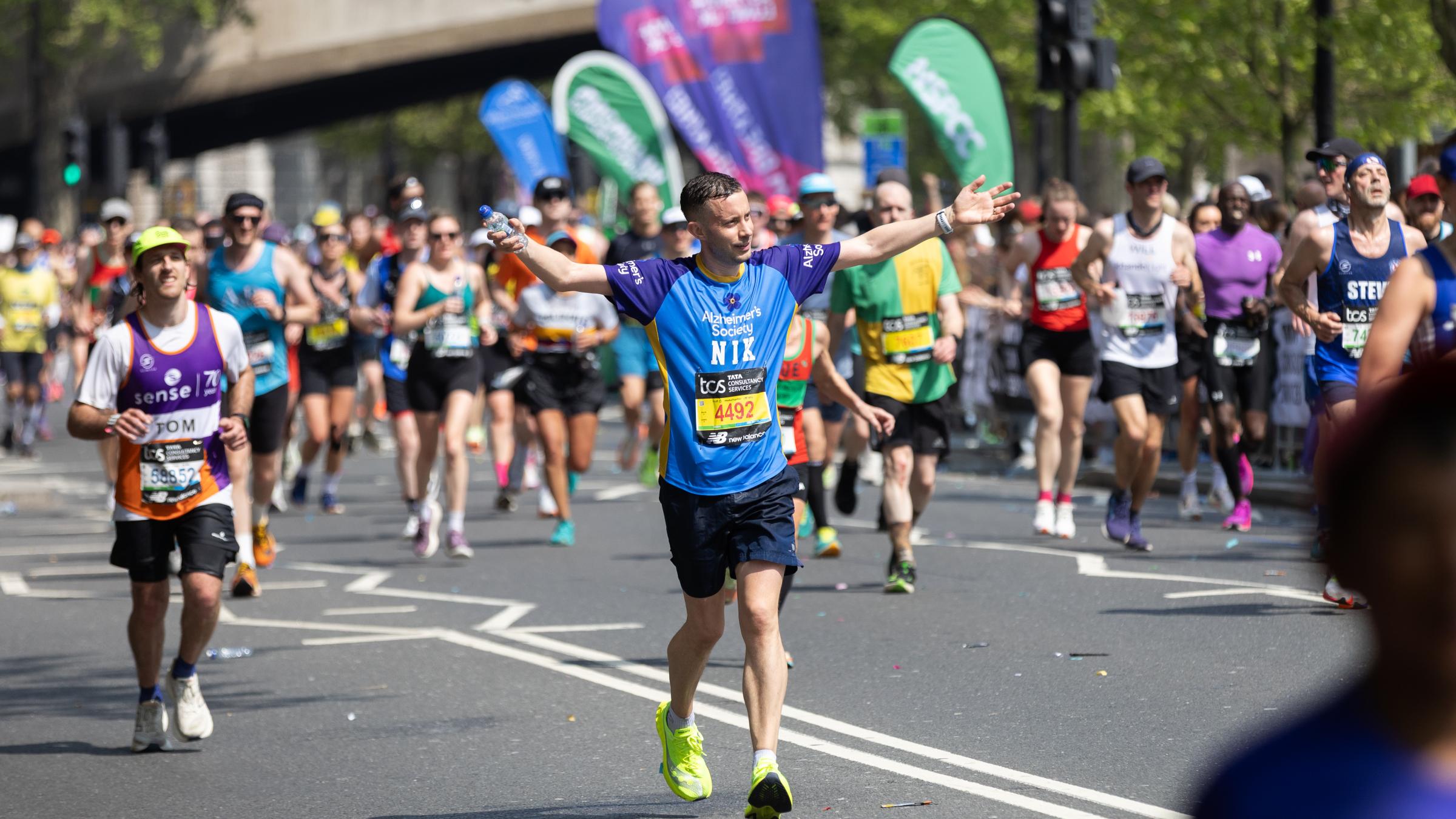 A runner waves while running along the London Marathon route. 