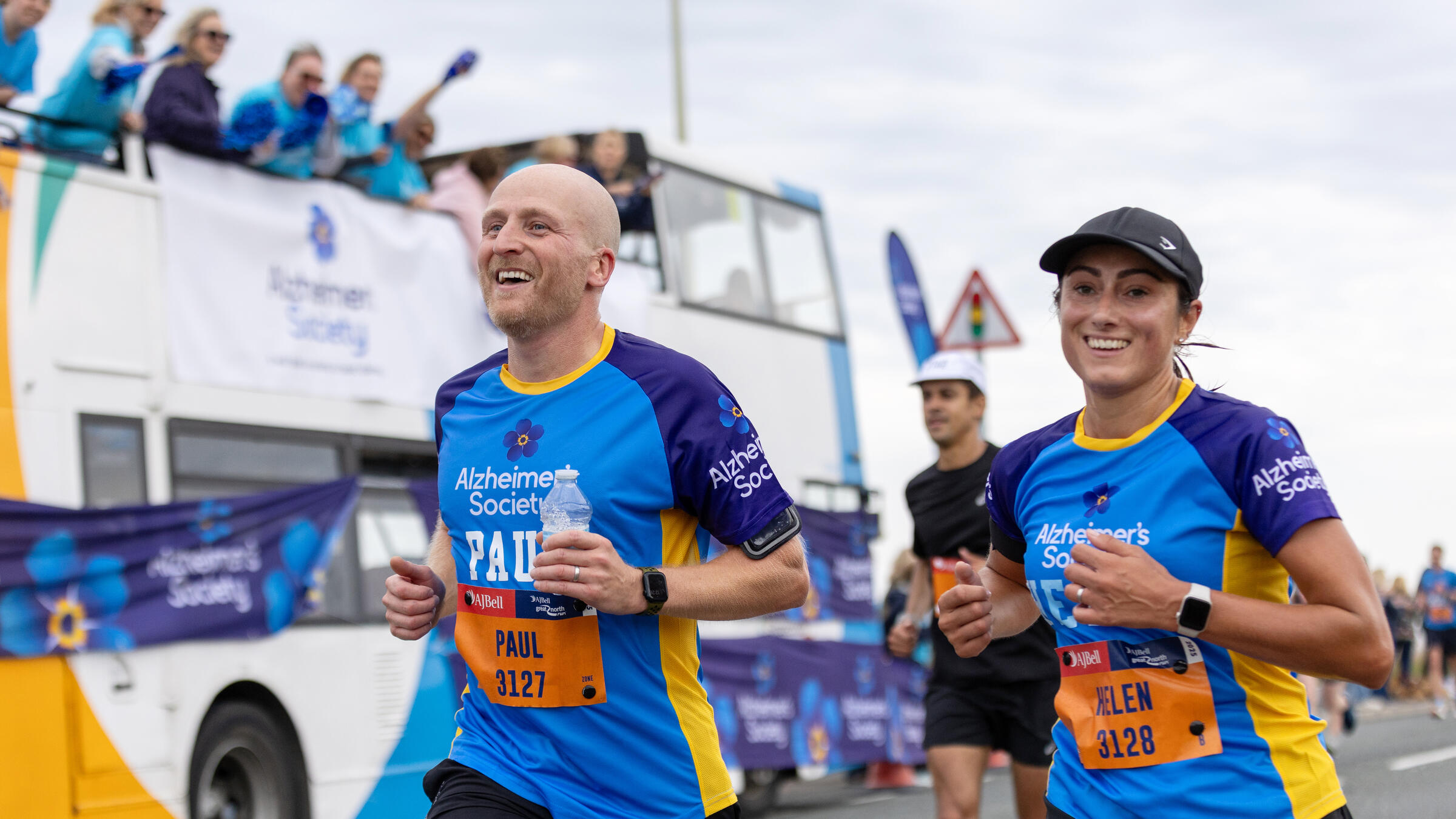 A man and woman run in front of an Alzheimer's Society branded bus