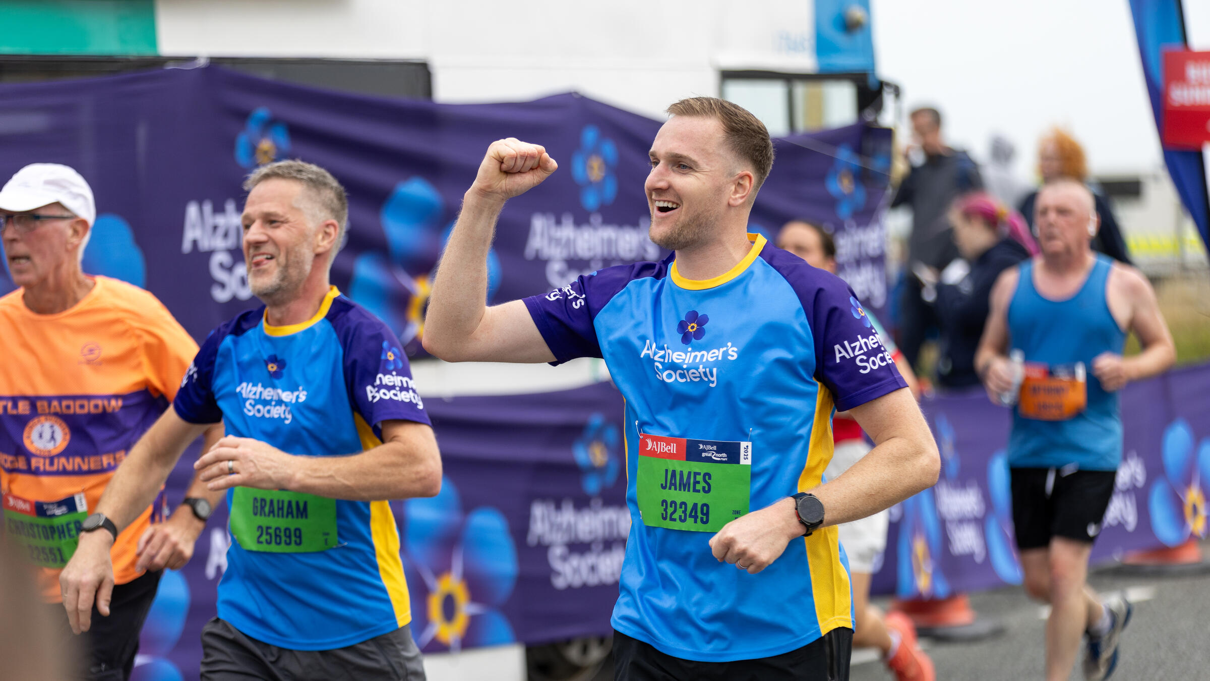 Two male runners in Alzheimer's Society branding, one is punching the air