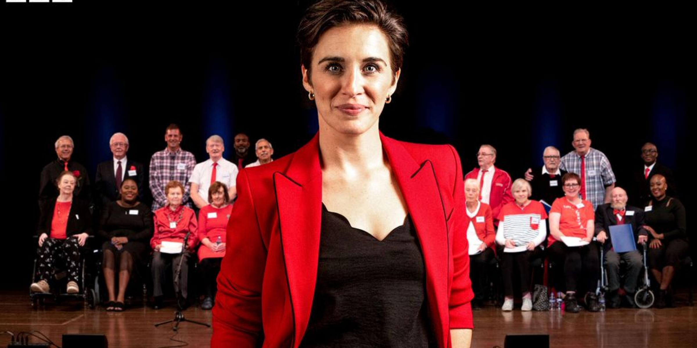 Vicky McClure smiling in the foreground with a choir of singers behind her