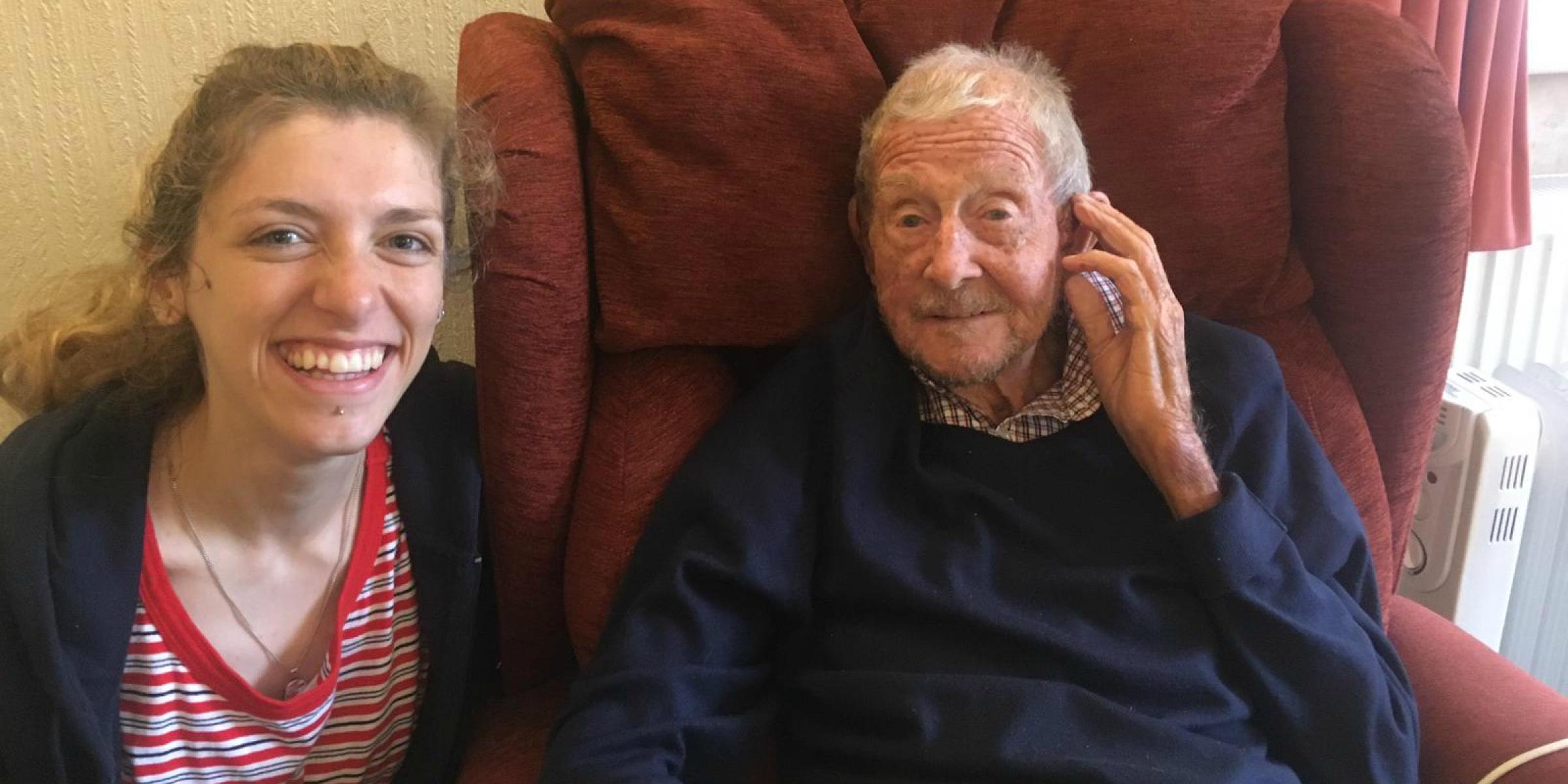 Ruby smiling beside her granddad, George, who sits in a red armchair