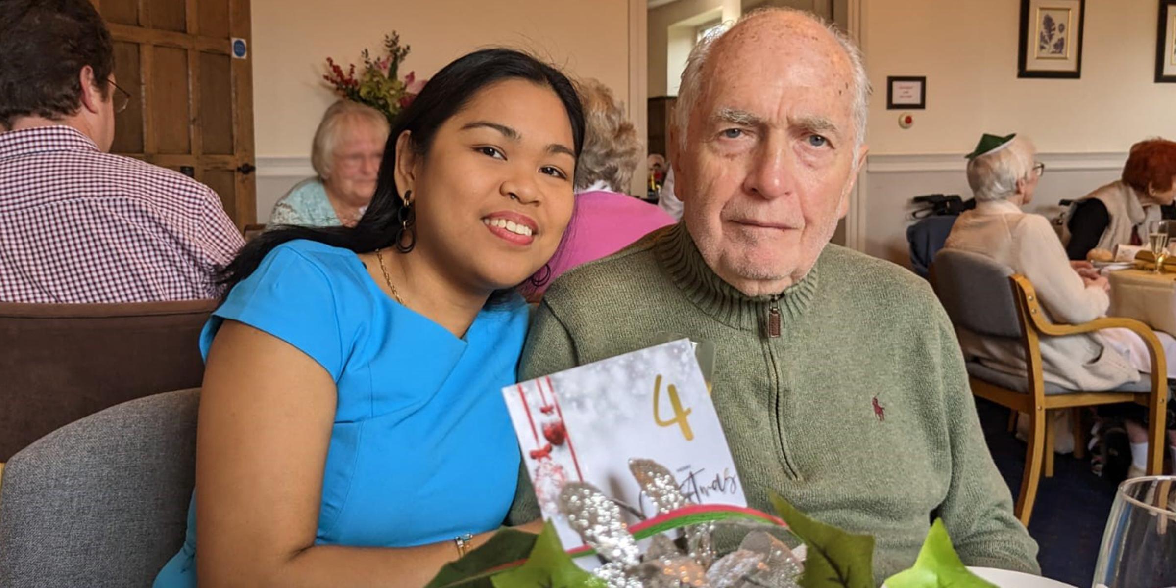 Daisy and Roy Timms sit next to each other in a restaurant at the table. They are both looking at the camera.