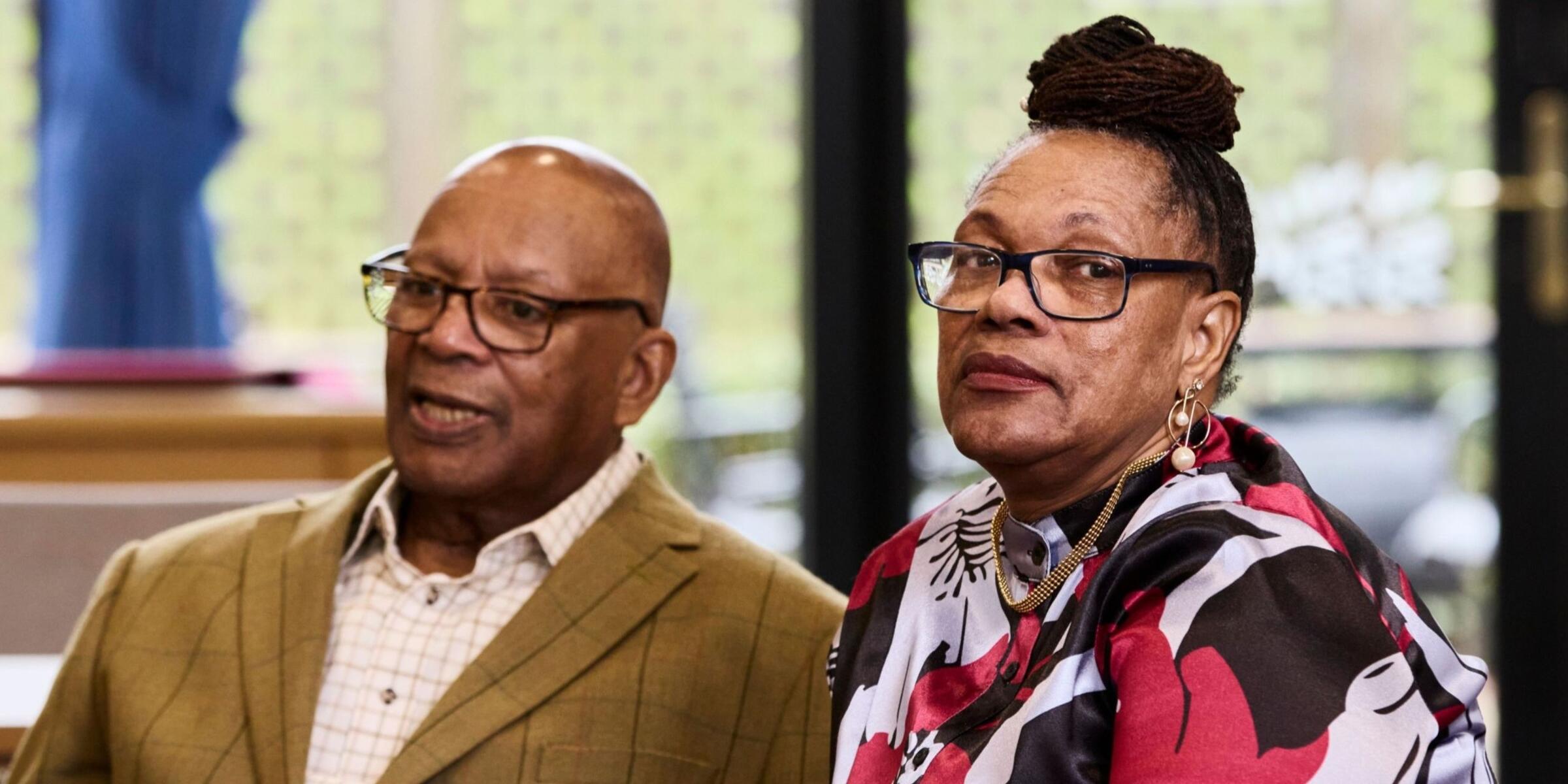 A man and woman sat at a table, the woman is looking at the camera