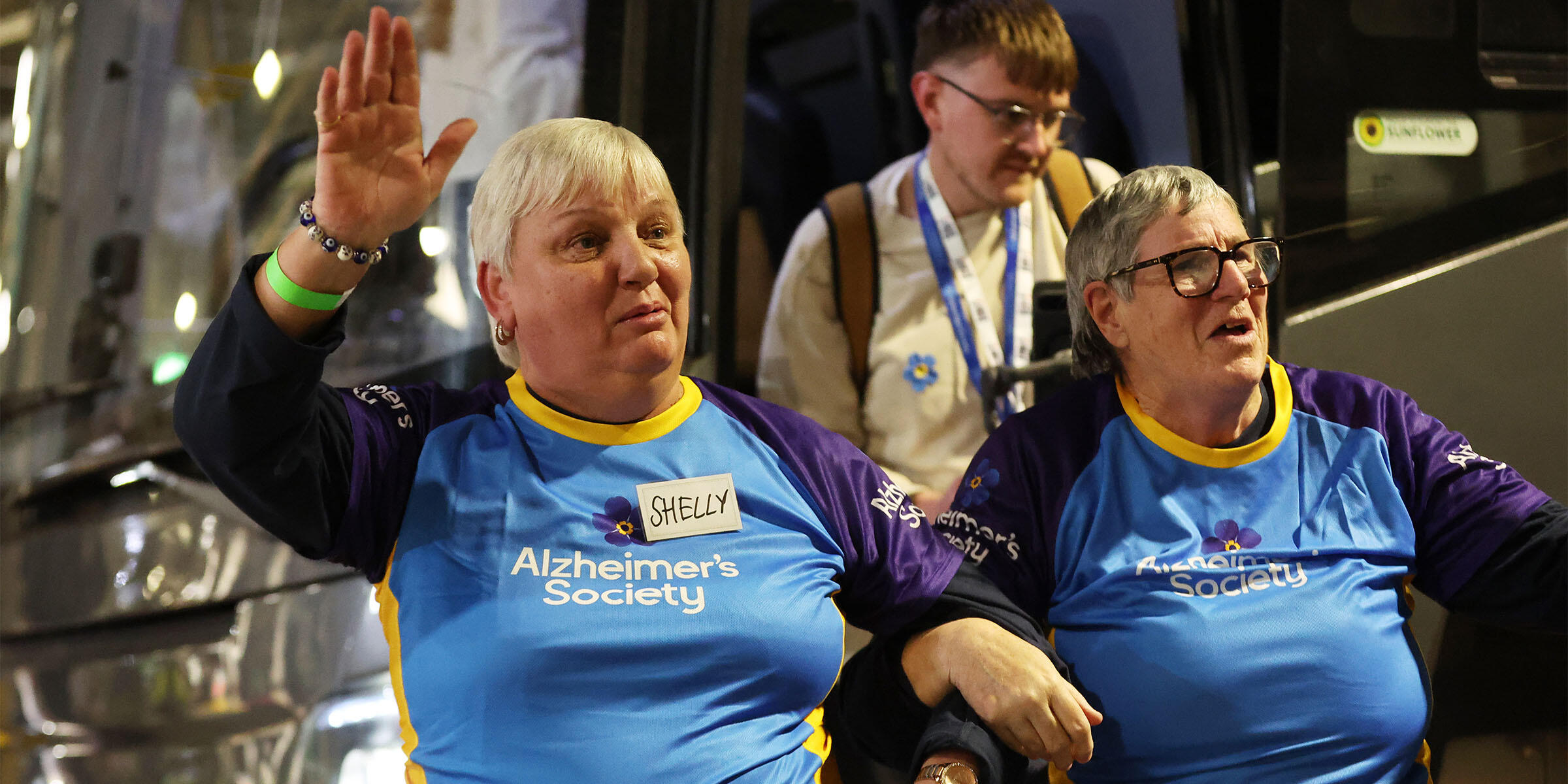 Susan and Shelly both have short grey hair, they're wearing blue Alzheimer's Society t-shirts and waving